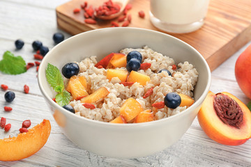 Bowl with oatmeal, peaches and berries on table