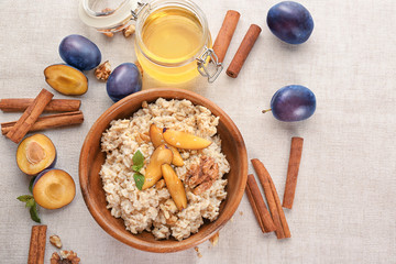Bowl with oatmeal, fresh plums and nuts on table