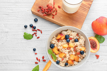 Bowl with oatmeal, peaches and berries on table