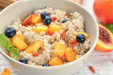 Bowl with oatmeal, peaches and berries on table