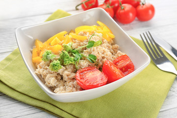 Bowl with oatmeal and vegetables on table