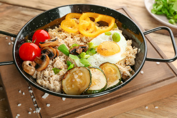 Frying egg with oatmeal, egg, mushrooms and vegetables on table