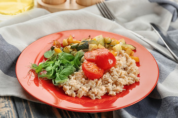 Plate with oatmeal and vegetables on table