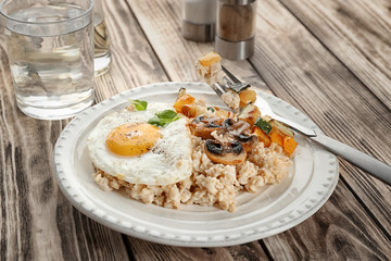 Plate with oatmeal, fried egg and vegetables on table