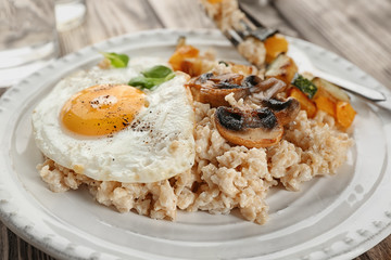 Plate with oatmeal, fried egg and vegetables on table
