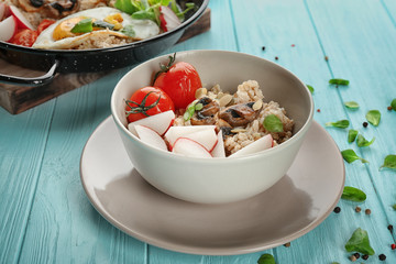 Bowl with oatmeal, mushrooms and vegetables on table