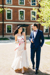 Naklejka premium Beautiful young bride in white wedding dress, holds bouquet, has talk with her future husband, have walk together, go to registry office. Lovely married couple rejoice special day in their life.