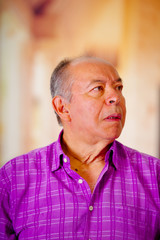 Portrait of a happy mature man wearing a purple square t-shirt in a blurred background