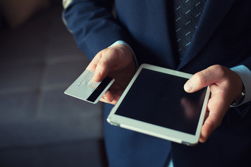 young businessman in dark office with smartphone tablet and credit card