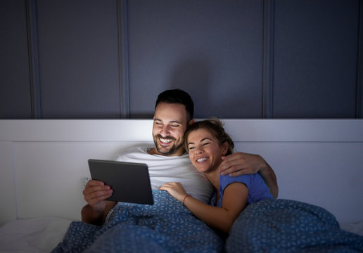 Close up of a beautiful smiling love couple lying on the bed and looking in a tablet together.