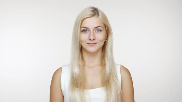 cute young blond blue-eyed girl looking at camera smiling over white background. Concept of emotions