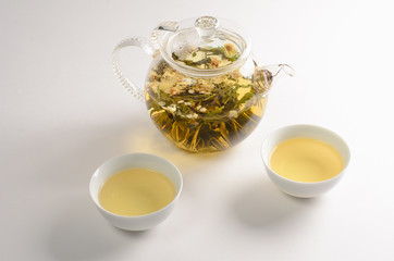 Green tea with flowers in glass teapot and two cups of tea on white background
