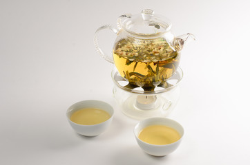 Green tea with flowers in glass teapot and two cups of tea on white background