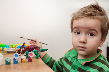 Little boy concentrating whilst painting a toy dinosaur on the desk