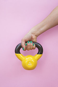 studio image of arm lifting colourful yellow kettle bell weight against a pink background
