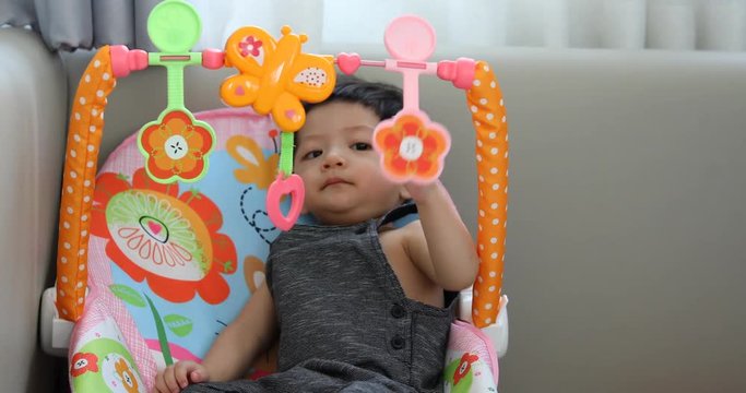 cute baby boy using finger hand playing colorful toy hanging overhead in nursery room