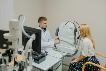 Young beautiful doctor/eye specialist/optometrist in an ophthalmologic clinic dooing a patient a...
