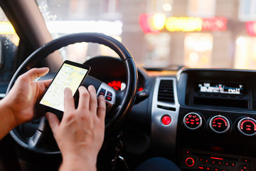 Closeup of smartphone in hand of young man sitting behind the wheel of modern car. In the...