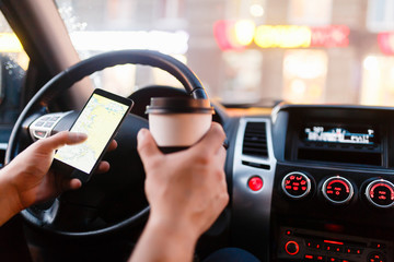 Driver with a smartphone in hand and paper cup of hot coffee in the driver's seat. The concept of inattention at the wheel, rest, coffee break to cheer. Man paves way in gps. On screen map of area.