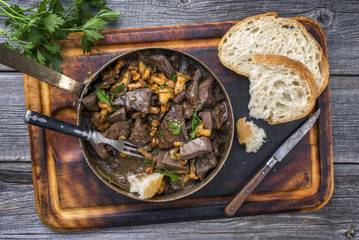 Fresh fried veal liver with chanterelle and baguette in sauce as top view in a casserole
