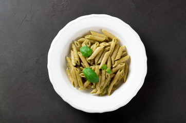 Pasta with homemade pesto sauce in a white plate on a dark stone slate background, top view, copy space