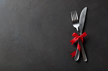 Festive set of cutlery knife and fork with red satin bow, dark stone slate background, top view, copyspace