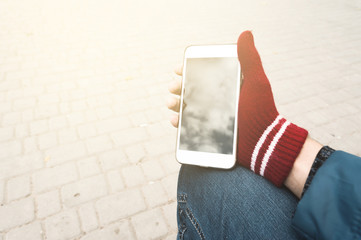 Man hand using a smart phone with red gleves and warm instagram filter outdoors. The man sitting and wait for the meeting with a person