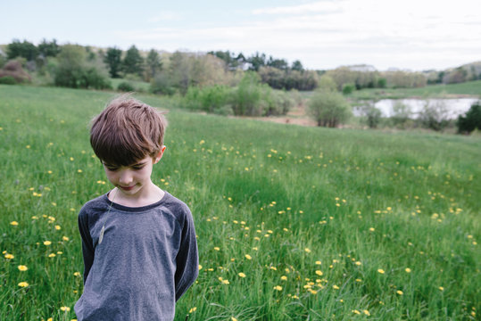 Little boy stands in field with grass in his mouth