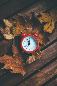 Autumn leafs and alarm clock on wooden table