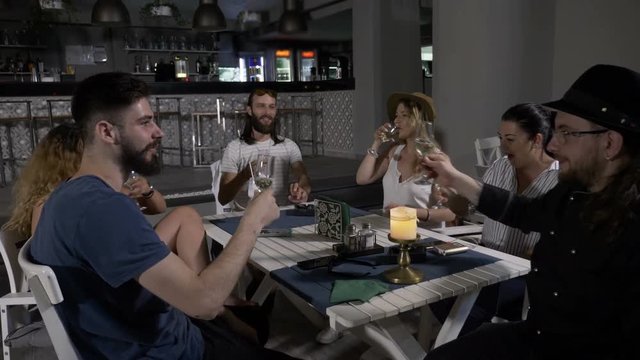 Group of happy millennials friends sitting at table in restaurant lounge toasting and clink glasses