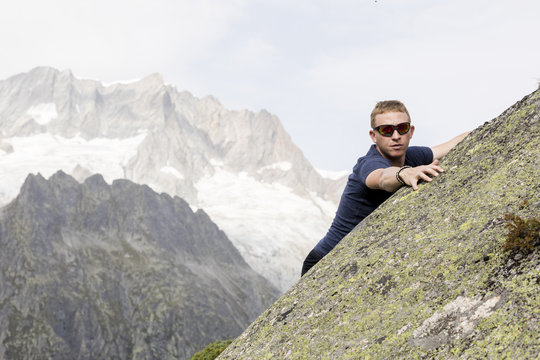 A climber makes climbing exercises on a big rock. In the background, the breathtaking mountain scenery of the Alps