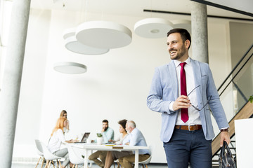 Young businessman leaves a meeting while other people stay in office