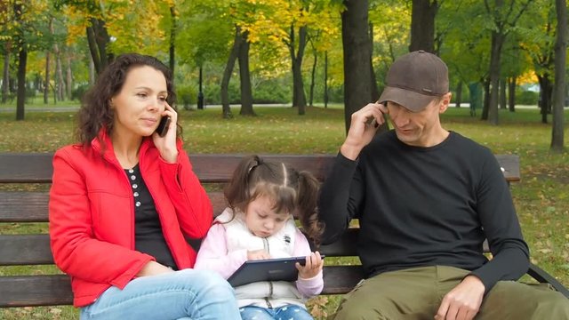 Family park with gadgets. Parents with a child with an autumn park with phones and a tablet.