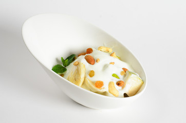 Fruit salad with yogurt and nuts in a bowl on white background