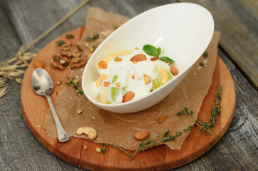 Fruit salad with yogurt and nuts in a bowl on desk on wooden background