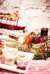 Christmas and New Year compsition of a gift, decor and a cup of cappuccino with candles and warm clothes in background