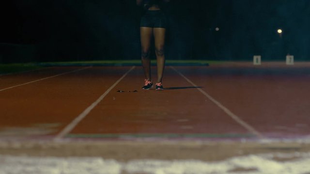  Female long jumper training at athletics track in the dark & rain. Slowmo
