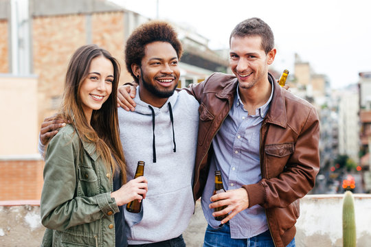 Portrait of happy young friends drinking bottles of beer on a rooftop.