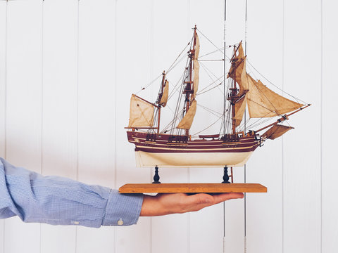 Man holding antique wooden ship replica.