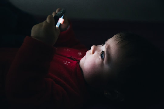 Baby using a mobile phone lying down on a bed
