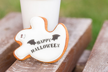 Halloween homemade gingerbread and honey cookies  as a white ghost with happy halloween greetings text on a wooden bench and cup of coffee on the background