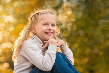 Happy girl playing in a beautiful autumn Park on a warm Sunny autumn evening. Girl 7 years old sits on blurred background with bokeh. Back light. The sun in your hair.
