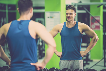 The happy sportsman look in the mirror in the fitness club