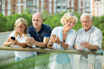 Portrait of positive mature couples using gadgets in park