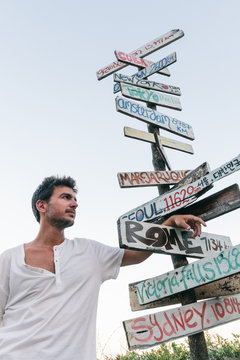 Young man next to a signpost with directions and distance to various countries