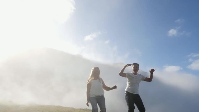 Young couple jumping on a mountain meadow on the background of fog and sun.