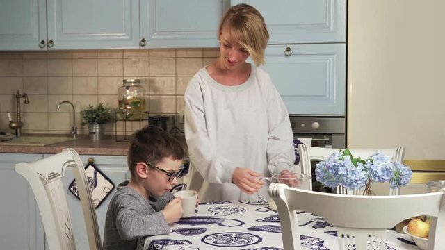 Mother pours milk into a mug and gives to drink to her son