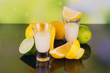 Glasses of cream liqueur with lime and lemon on green background with reflection.
