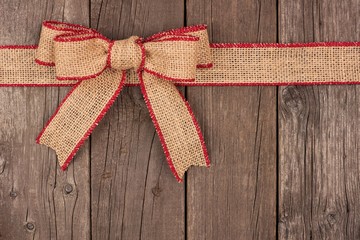 Burlap Christmas bow and ribbon top border, above view on a rustic wood background