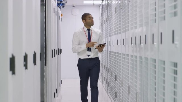 IT engineer with computer tablet checking the servers in a data center. Two businessmen taking a look round in the background.